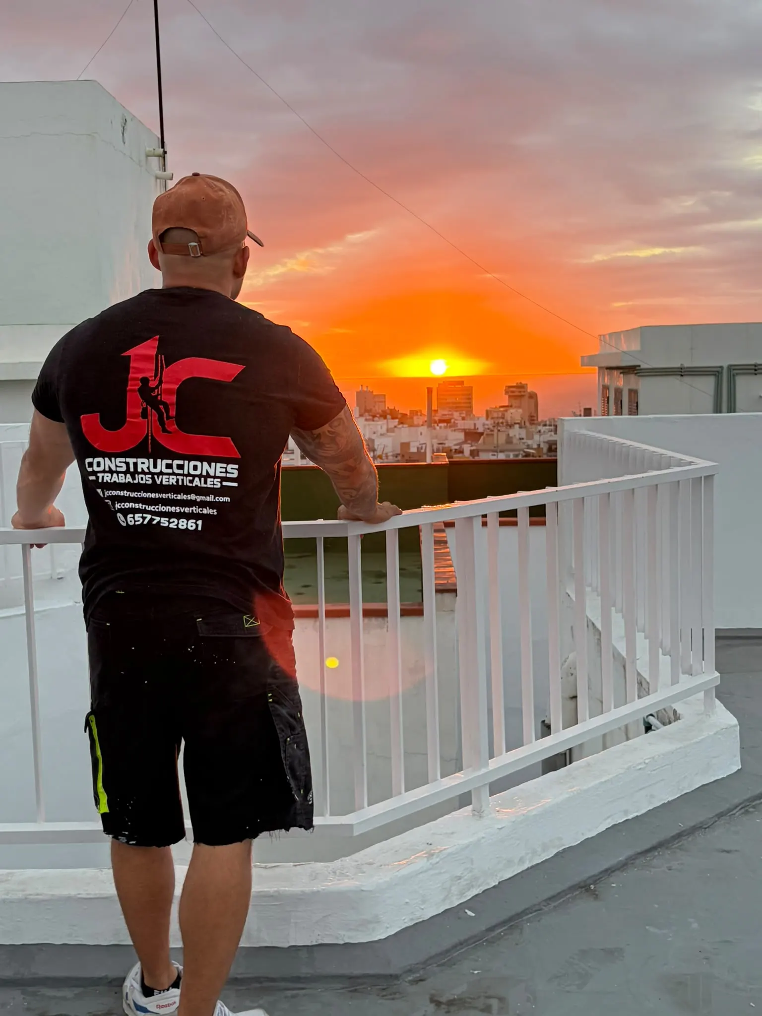 Cristofer González, de espaldas con la camiseta de JC Construcciones, mirando el atardecer desde una azotea recién terminada